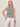A woman with blonde hair wears the Sanctuary Clothing campari tank macrame stripe top and white lace-up pants, standing against a plain light background with a brown bangle on her wrist.