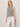 A woman models the Sanctuary Clothing campari tank macrame stripe, a sleeveless black-and-white striped top, paired with white lace-up pants against a plain light background, her head slightly tilted and one hand at her side.