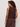 A woman with curly hair is seen from the back, wearing Sanctuary Clothing’s retreat bubble tank in rich soil—a sleeveless dark brown top with a keyhole—paired with matching loose brown pants against a plain light background.
