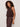 A woman with curly hair models the Sanctuary Clothing retreat bubble tank in rich soil, a sleeveless dark brown top paired with matching pants, standing sideways against a plain light background.