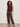 A woman with curly hair stands confidently in Sanctuary Clothing's retreat bubble tank in rich soil, paired with matching loose drawstring pants and sandals, against a plain light wall.