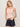 A woman with blonde hair models the Sanctuary Clothing sprinter rib tank in bleached pink, paired with dark denim shorts and a tan belt, standing against a plain light background with her hands in her pockets.