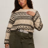 A woman with curly hair wears the Sanctuary Clothing fairisle sweater in light oat multi (extended sizing), tucked into high-waisted olive green pants with a belt, standing against a plain light background.