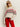A woman models the Sanctuary Clothing send it sweater chalk multi€�featuring red and black geometric patterns€�with red pants and sunglasses, standing against a plain light background with one hand in her pocket.