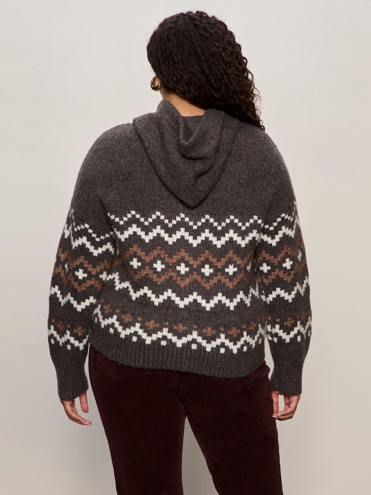A person with long curly hair is seen from the back, wearing Sanctuary Clothing„¢s zip up fairisle hoodie mocha fairisle extended sizing and dark pants.