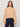 A woman with long brown hair wears the Sanctuary Clothing Forever Cashmere Popover in toasted beige and dark blue high-waisted jeans, standing against a plain, light background.