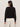 A woman with long dark hair, seen from behind, wears the Sanctuary Clothing "for keeps pointelle cardigan" in black with white pants, standing against a plain light-colored wall.
