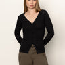 A woman with straight, light brown hair models the Sanctuary Clothing fitted raglan cardi in black, paired with olive green pants, against a plain light background.