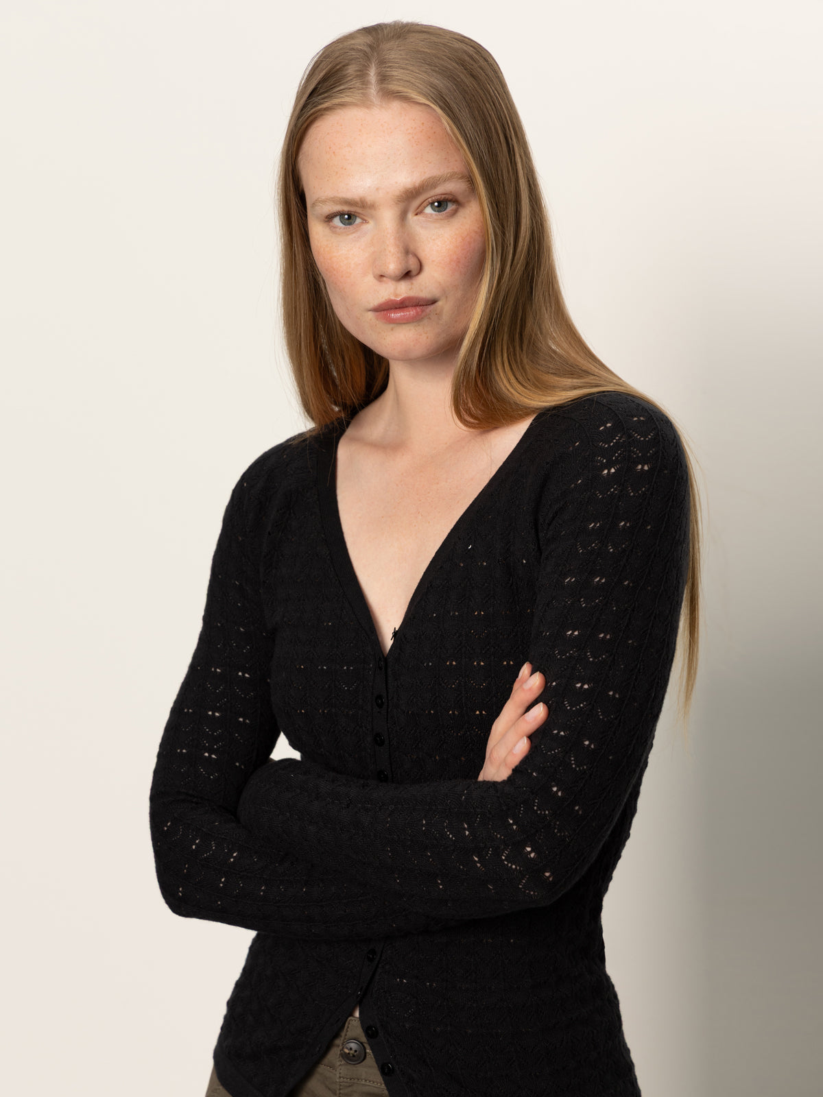 A woman with long straight blonde hair wears the fitted raglan cardi black by Sanctuary Clothing and olive pants, standing with her arms crossed and looking at the camera against a plain light background.