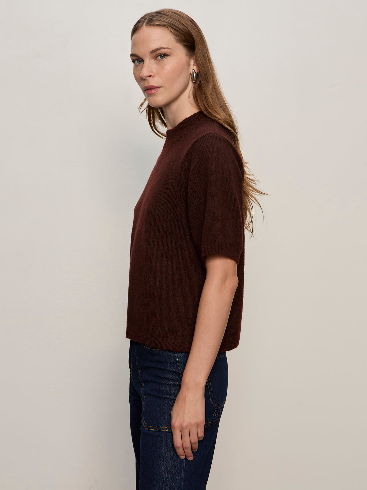A woman with long light brown hair wears the Sanctuary Clothing perfect sweater tee in dark crimson and dark blue jeans, standing in profile against a plain light background.