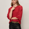A woman with straight, light brown hair wears the Sanctuary Clothing ribbed sweater tee in cherry lacquer, styled with black leather pants, a leopard print belt, and gold jewelry against a plain light backdrop.