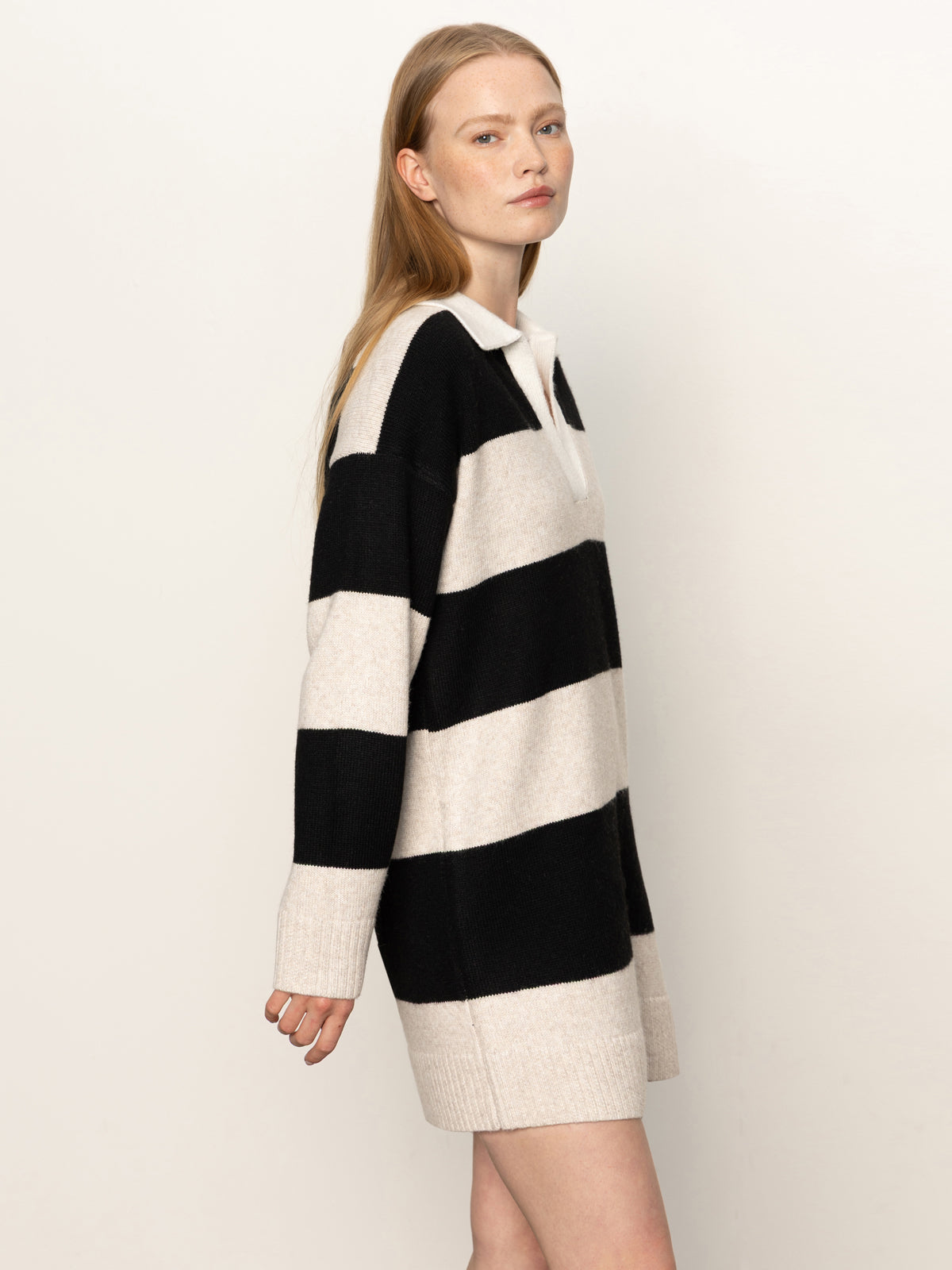 A woman with long, straight blonde hair models the Sanctuary Clothing polo striped sweater dress in heather pearl with black, standing against a plain light background and looking slightly to the side with a neutral expression.