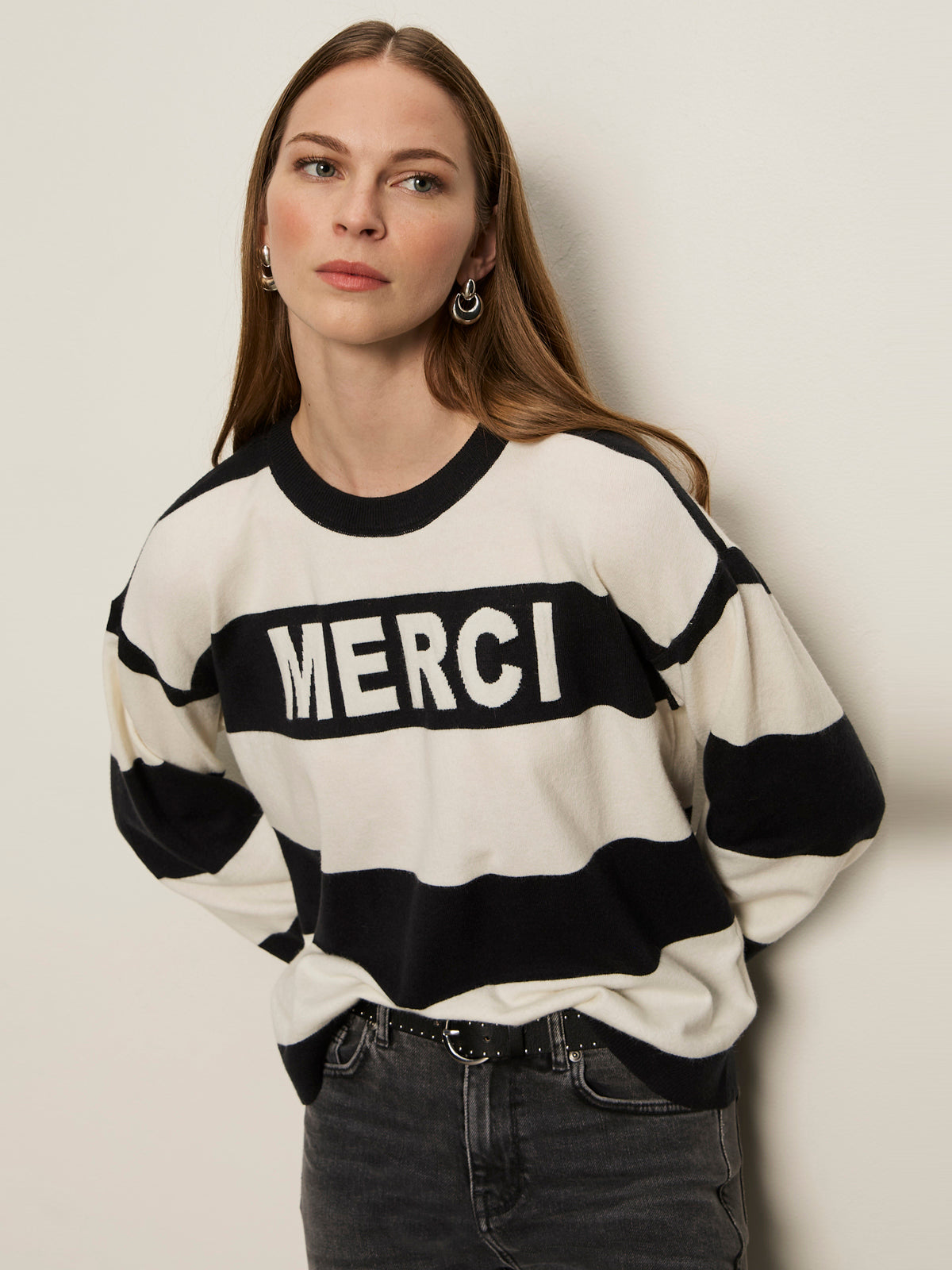 A woman with long brown hair wears Sanctuary Clothing„¢s 24 7 Popover Black with Chalk Stripe sweater. She stands against a light background, looking to the side with a neutral expression.