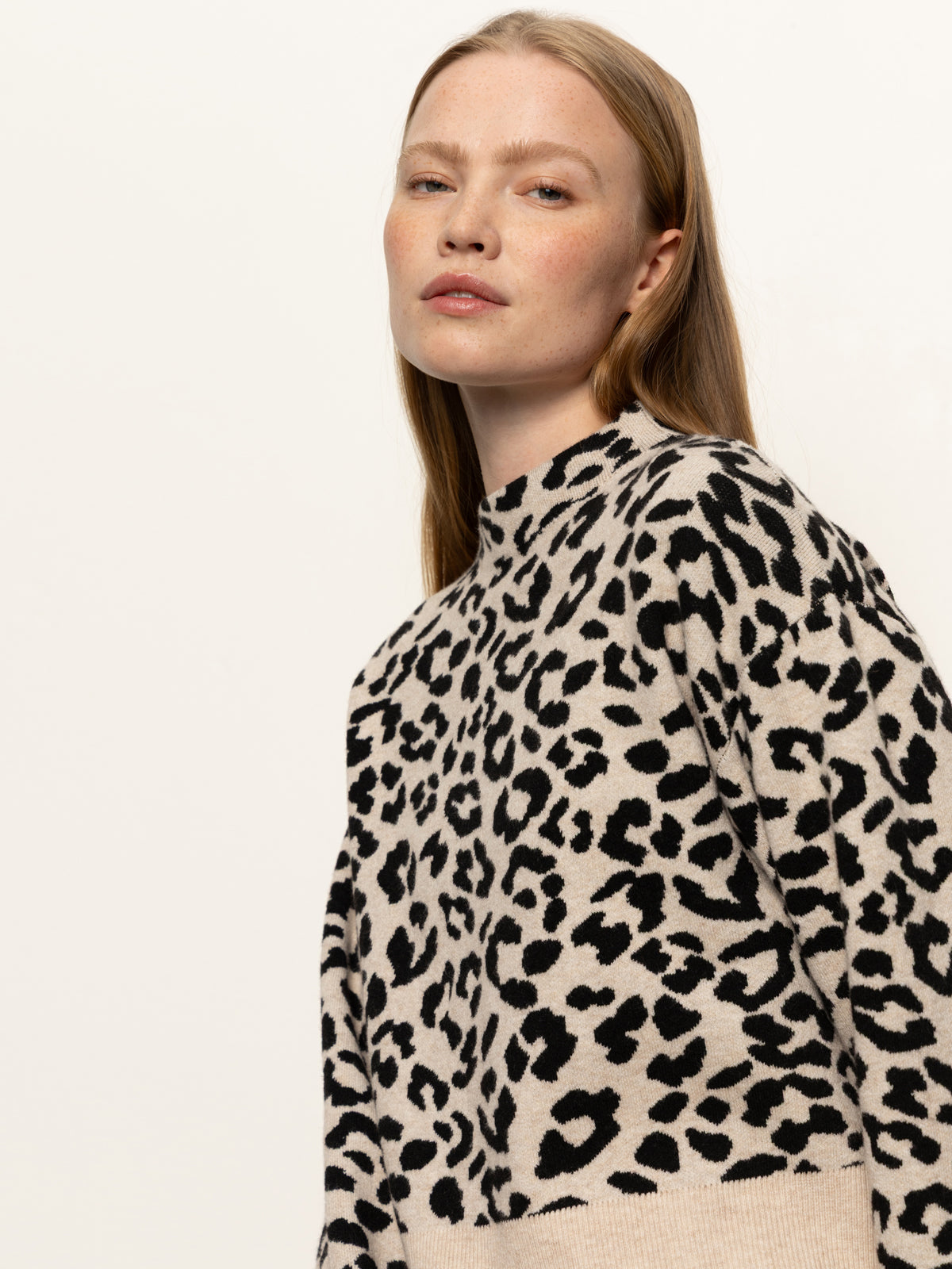 A person with long, straight hair wears the Sanctuary Clothing "soft touch popover spots" sweater in a beige and black leopard print, confidently facing the camera against a plain, light background.