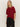 A woman with straight blonde hair wears the Sanctuary Clothing short sleeve shine sweater tee in cherry lacquer shine and black pants, standing against a plain light background with her hands in her pockets.