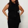 A woman with curly hair wears the Sanctuary Clothing scarf sweater shell in black extended sizing, paired with black pants, standing against a plain white background with her hands on her hips.