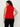 A woman with curly dark hair models the Sanctuary Clothing scarf sweater shell in cherry lacquer (extended sizing), a sleeveless red turtleneck, paired with black pants, standing with her back to the camera against a light background.