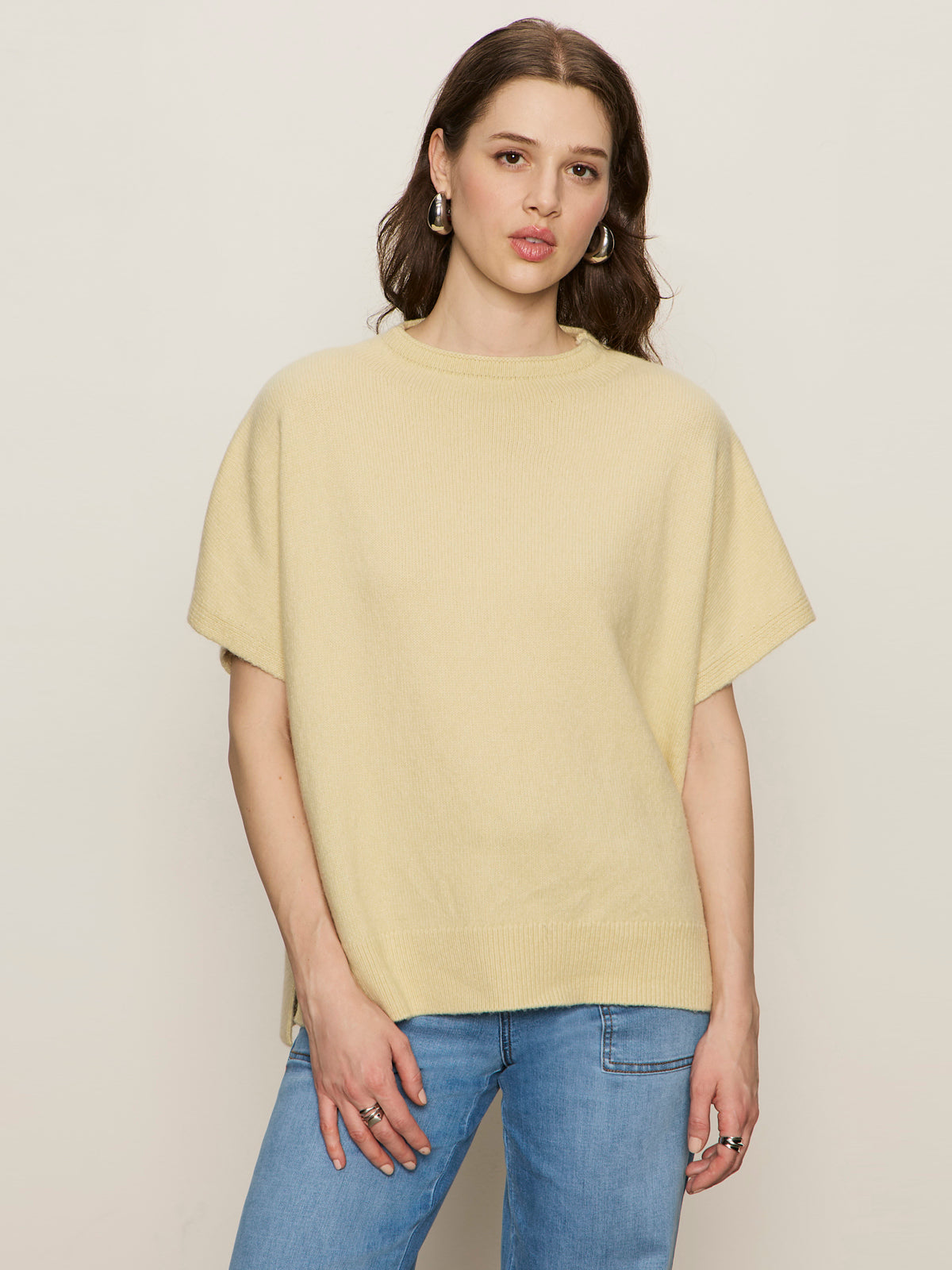 A woman with long brown hair, wearing the Sanctuary Clothing easy layering shell in buttercream, stands against a plain light background, looking at the camera with a neutral expression.