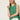 A woman with long blonde hair wears the Sanctuary Clothing easy pointelle shell in green juice and white pants, standing against a plain light-colored background and looking slightly upward.