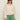 A woman wears the Sanctuary Clothing daily escape flower pop bomber collagen over a white top with high-waisted green pants, standing against a plain light background, hands relaxed by her sides.