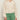 A woman wears the Sanctuary Clothing daily escape flower pop bomber in collagen petite sizing over a white top and high-waisted green jeans. The cream-colored knit cardigan features a subtle pattern; image cropped from shoulders down.