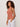 A woman with curly hair wears the Sanctuary Clothing "in the mix sweater tank" in ancient clay and white drawstring pants, standing against a plain light background with her hands in her pockets, gazing to the side.