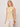 A woman with shoulder-length blonde hair wears the Sanctuary Clothing "in the mix sweater tank banana," a sleeveless, light beige ribbed top, and off-white pants. She stands against a plain background, looking slightly to the side, with two brown bangles on her right wrist.