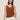 A woman with shoulder-length brown hair wears the Sanctuary Clothing dune studded tank in ancient clay and white pants, accessorized with yellow bracelets and a necklace, standing against a plain beige background.