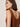 A woman with straight brown hair models the Sanctuary Clothing dune studded tank in ancient clay, a sleeveless, rust-colored knit top with bead details and a deep scoop back. She stands slightly turned away against a plain backdrop.