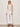 A woman in Sanctuary Clothing's summer shine sequin shell summer sand white stripe top pairs it with high-waisted white wide-leg pants and brown sandals, standing against a light wall.