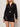 A woman wears the Sanctuary Clothing laguna openwork bomber in black (petite sizing) with a matching mini skirt, both featuring a sheer crochet knit. She has wavy blonde hair and accessorizes with a bangle bracelet.