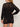 A person is seen from behind wearing Sanctuary Clothing's Laguna Openwork Bomber in black (petite sizing), revealing a black undergarment, paired with matching mini skirt, wavy light brown hair, and chunky bangles.