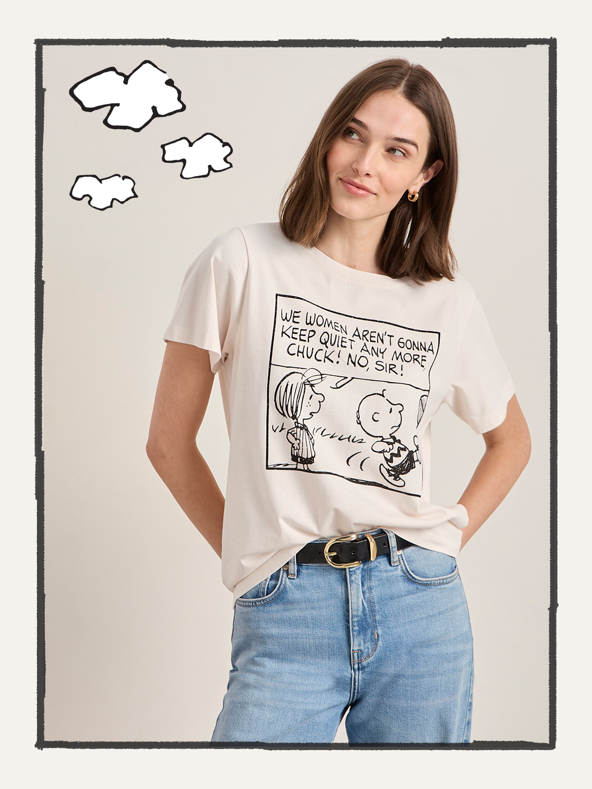 A woman in jeans and a pink "arent gonna keep quiet tee milk" by Sanctuary Clothing, featuring a cartoon print, stands smiling with one hand in her pocket against a white background with cloud doodles.