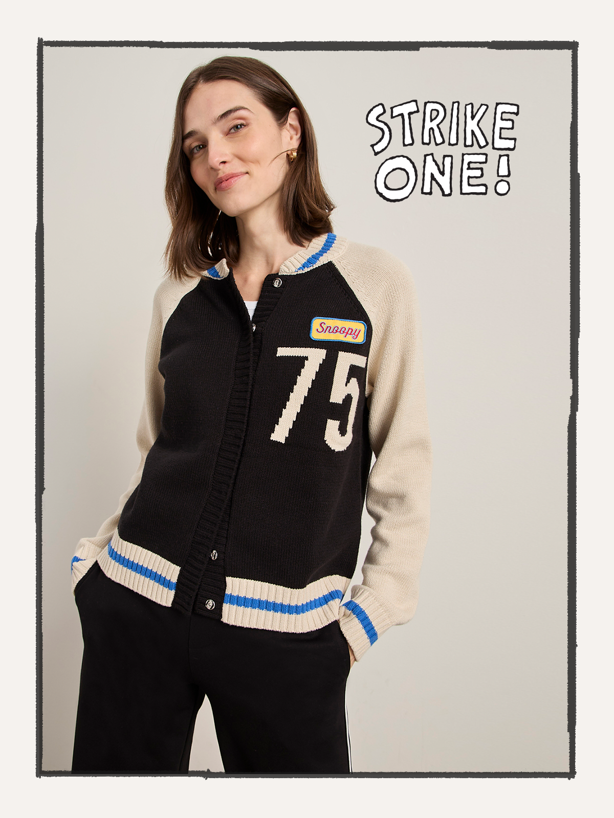 A woman with shoulder-length brown hair smiles with her hands in her pockets, wearing the Sanctuary Clothing 75 bomber sweater in black chalk. "STRIKE ONE!" appears beside her.