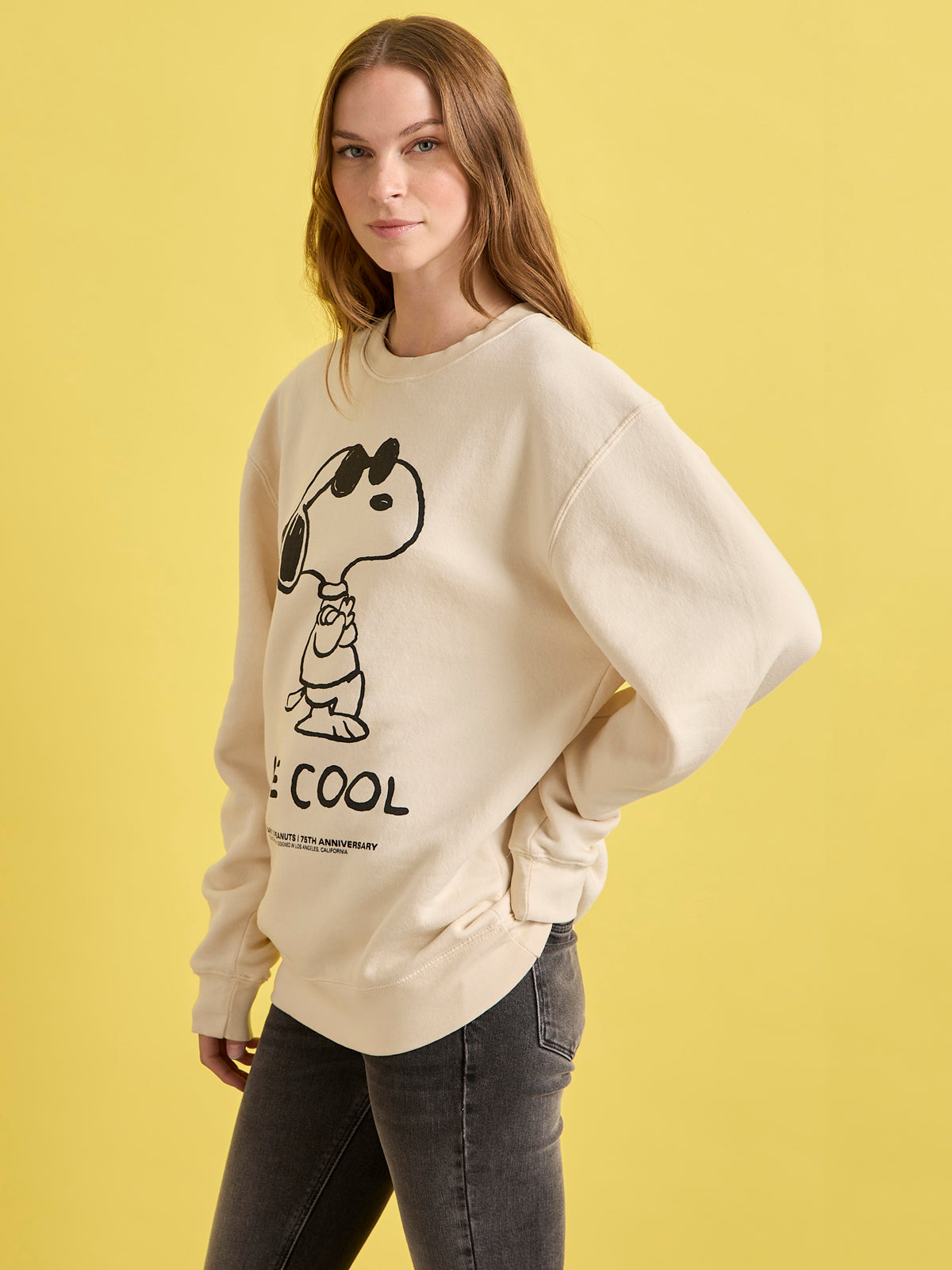 Woman wearing a beige sweatshirt with a graphic design on a yellow background