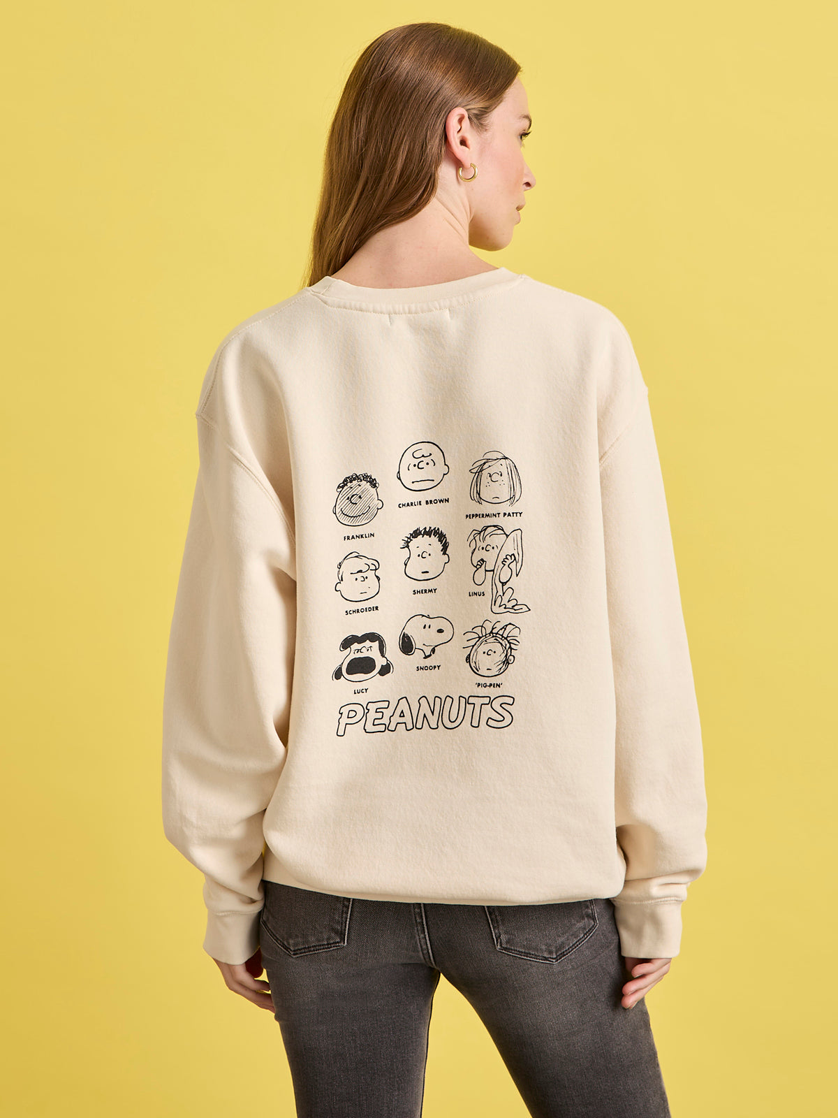 Person wearing a beige sweatshirt with Peanuts character illustrations on the back against a yellow background