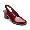 The opera sling back pump wine by Sanctuary Clothing features maroon patent leather, a rounded toe, block heel, and elasticized back strap, shown against a white background.