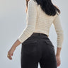 A woman with long dark hair, wearing a cream textured knit sweater and Sanctuary Clothingžs corduroy Hayden bootcut pant in Semi Sweet, stands with her back to the camera against a light neutral background.