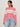 A woman wears the Sanctuary Clothing sporty openwork popover bloom pink with collagen stripe sweater and light blue jeans, standing against a plain light background.